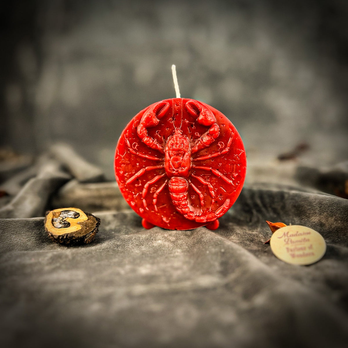 Deep red Scorpio medallion candle standing on its three small feet.