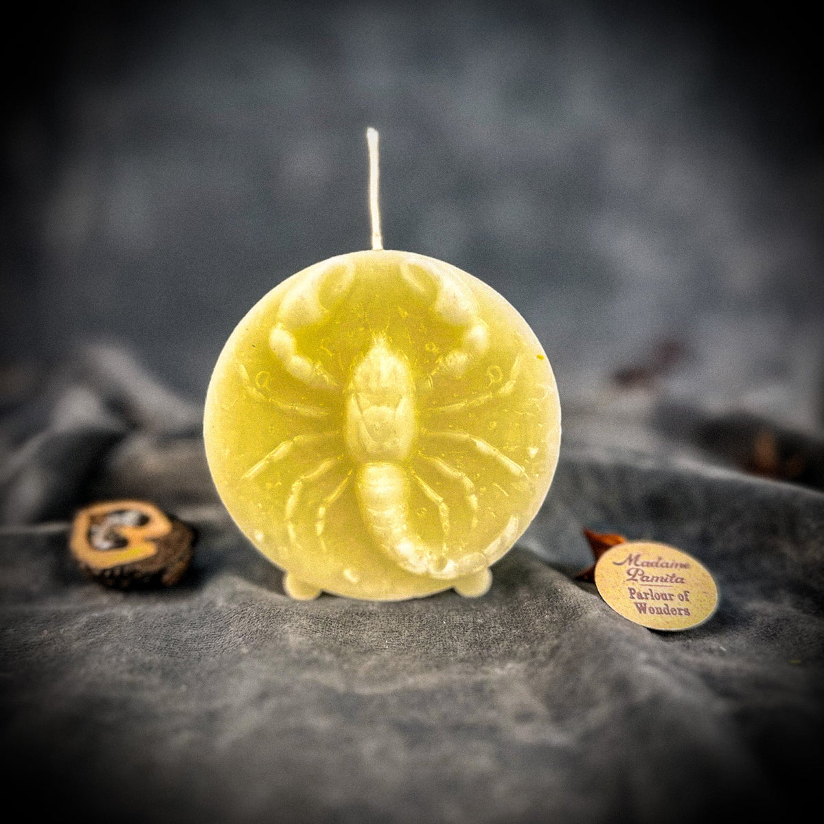 Pale yellow-green Scorpio medallion candle on gray velvet.