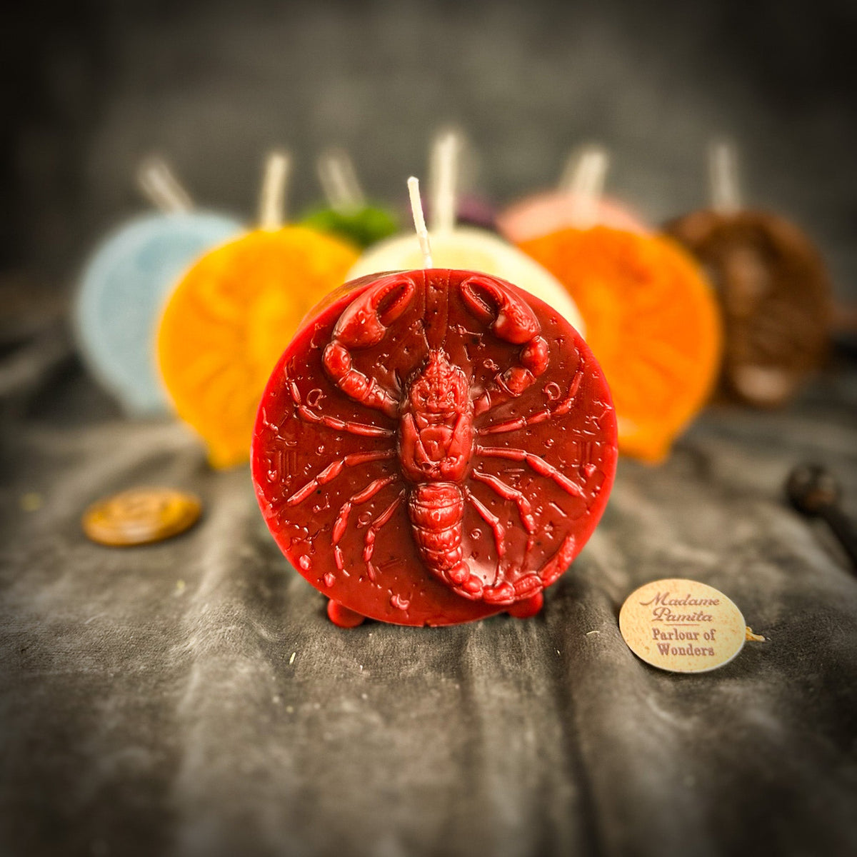 The red Scorpio medallion in front of the other colors on gray velvet, the Madame Pamita label at its foot.