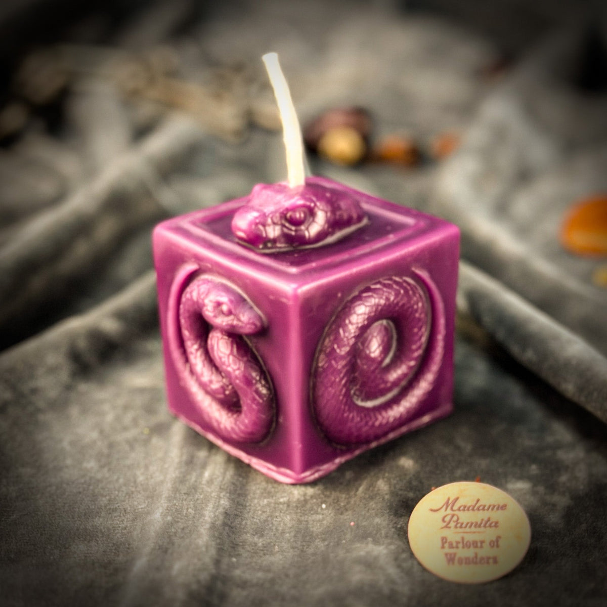 Snake of Transformation beeswax cube candle in deep pink on draped gray fabric