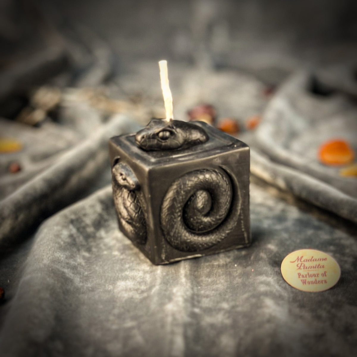Snake of Transformation beeswax cube candle in black on draped gray fabric