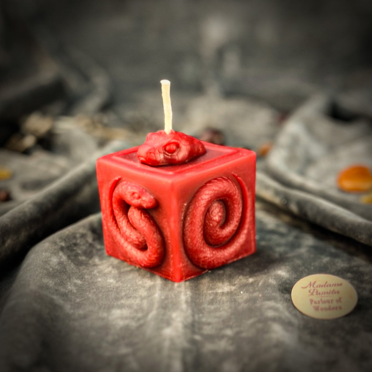 Snake of Transformation beeswax cube candle in red on draped gray fabric