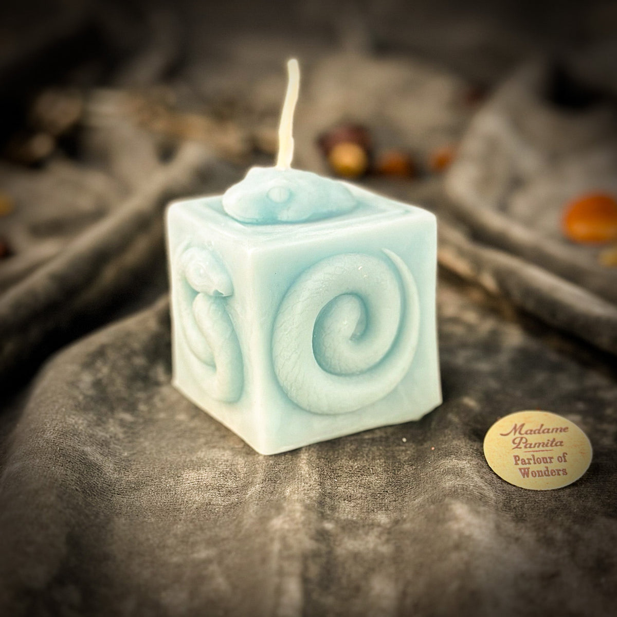 Snake of Transformation beeswax cube candle in pale blue on draped gray fabric