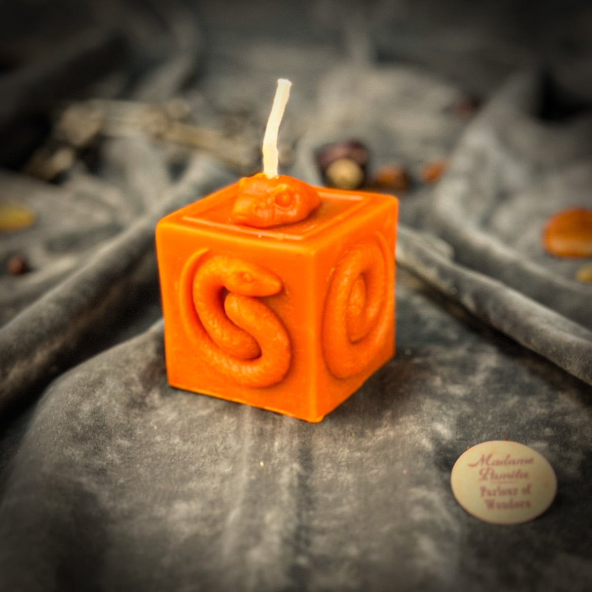 Snake of Transformation beeswax cube candle in orange on draped gray fabric