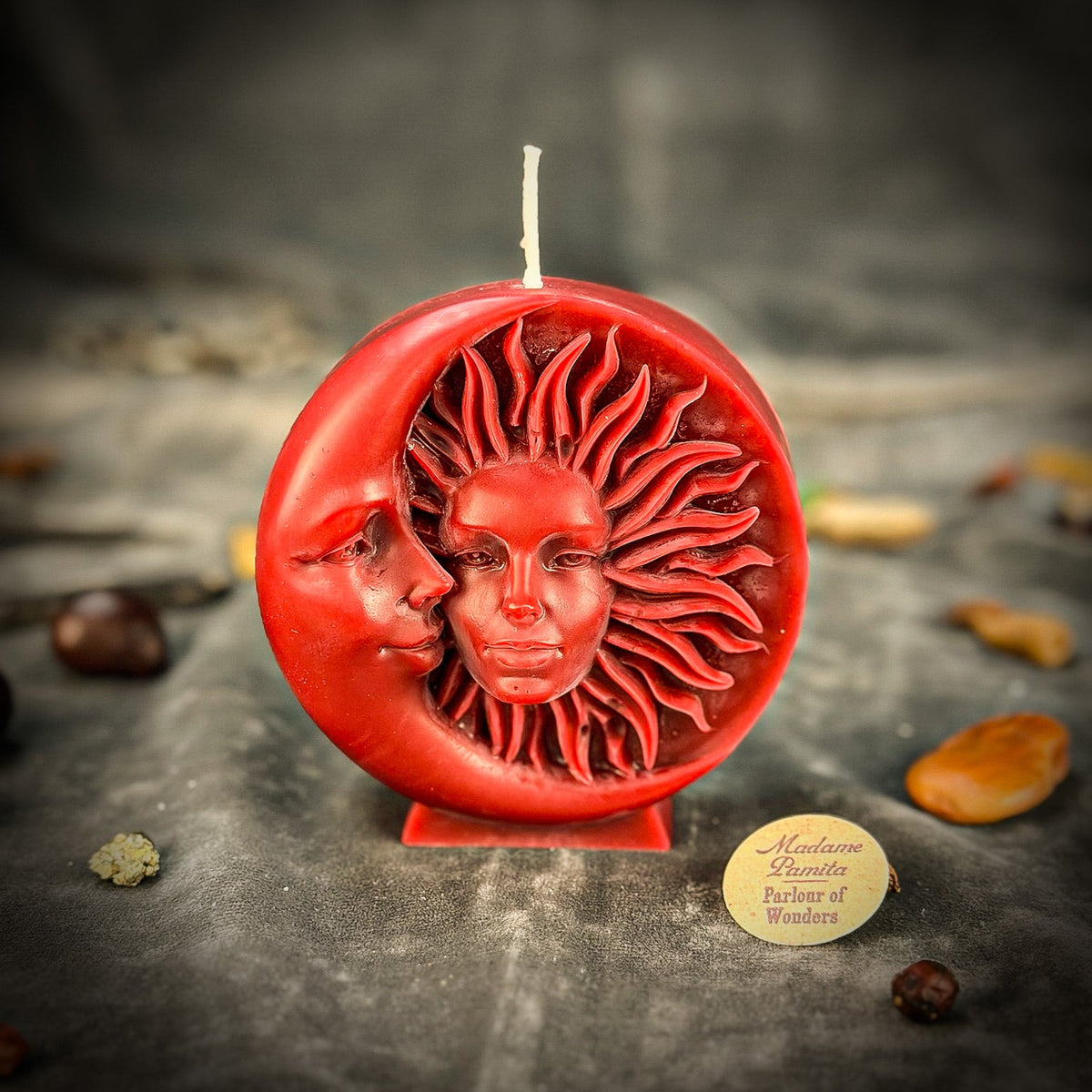 Red sun-and-moon disc candle on gray velvet with dried berries and seeds scattered around its foot