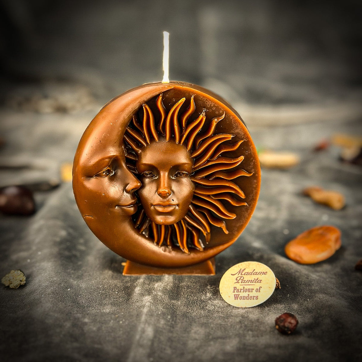 Copper-brown sun-and-moon disc candle on gray velvet, the relief faces gleaming with a metallic sheen