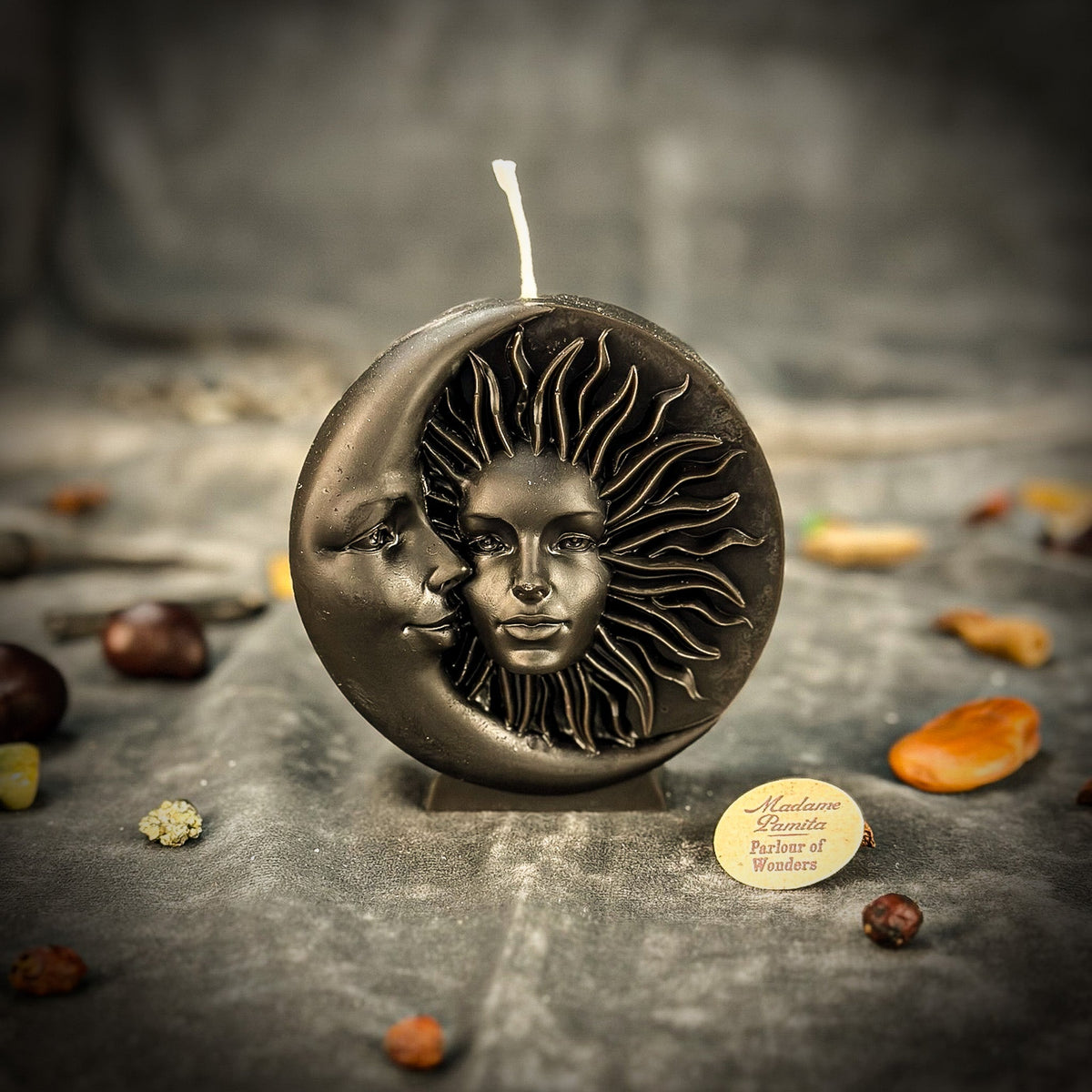 Black sun-and-moon disc candle on gray velvet, the carved faces catching a rim of light