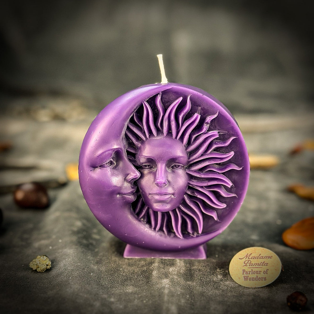 Violet sun-and-moon disc candle standing on gray velvet with the round maker's token beside it