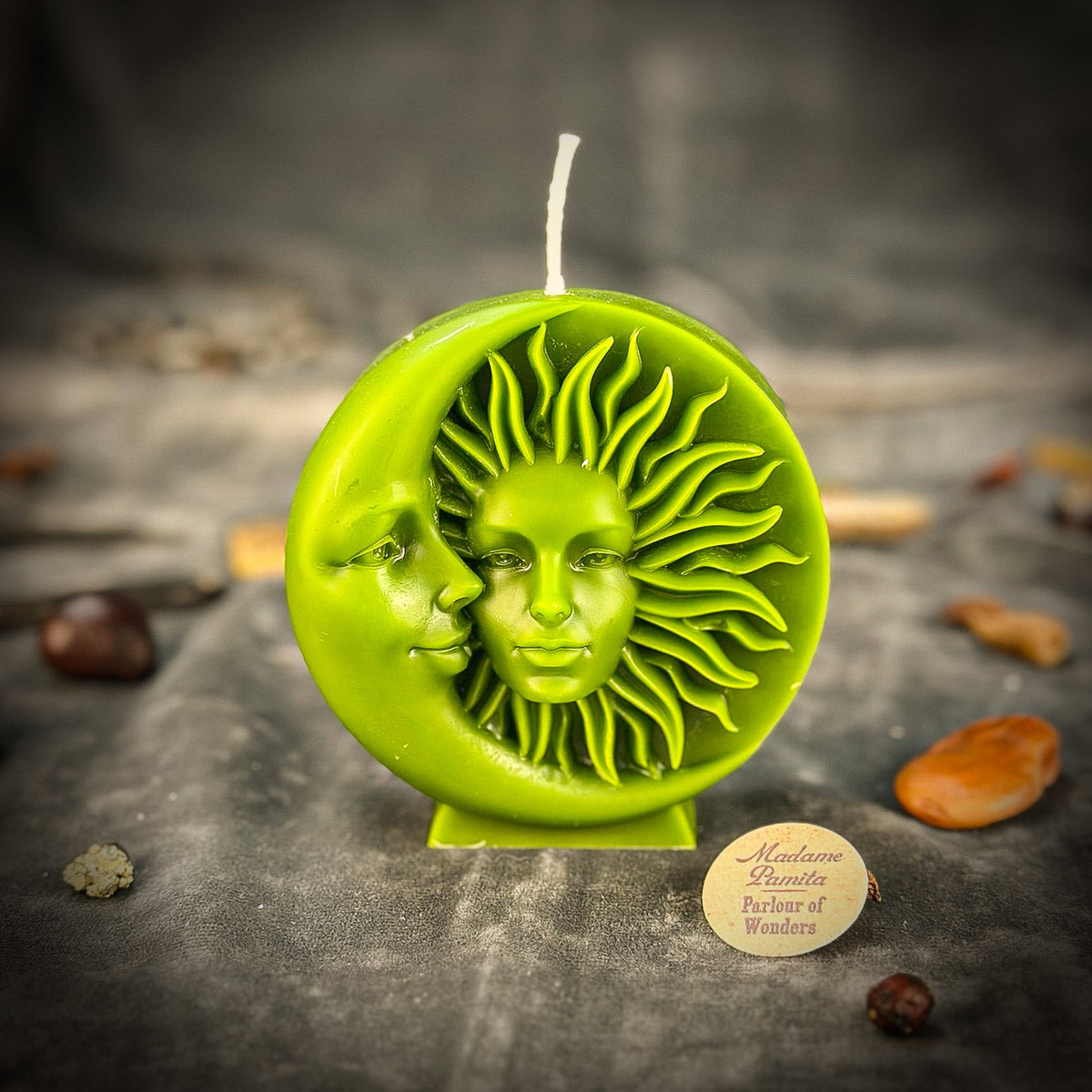 Lime green sun-and-moon disc candle standing on gray velvet with the Parlour of Wonders token in front