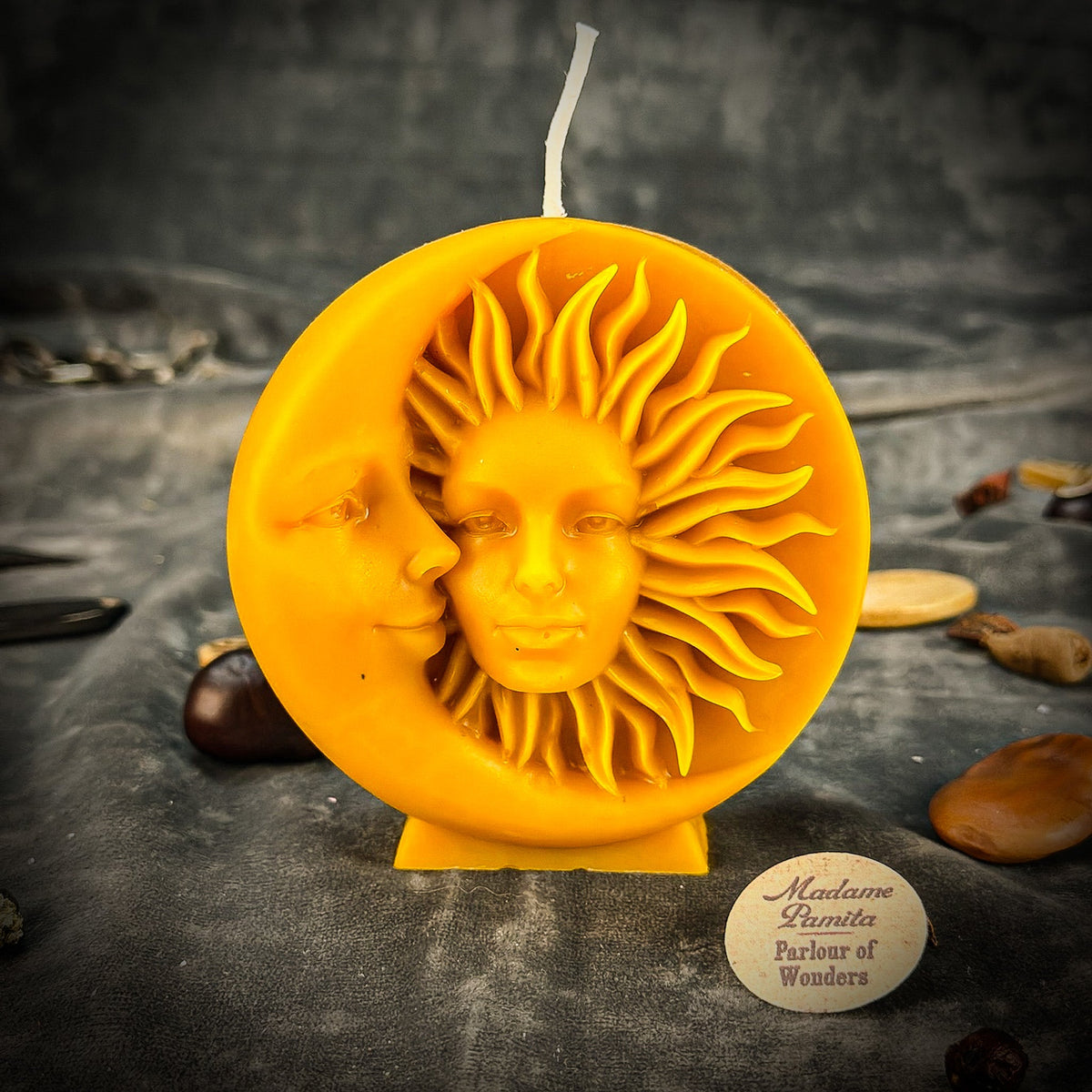 Golden yellow sun-and-moon disc candle standing on its cast foot on gray velvet, the Madame Pamita Parlour of Wonders token in front