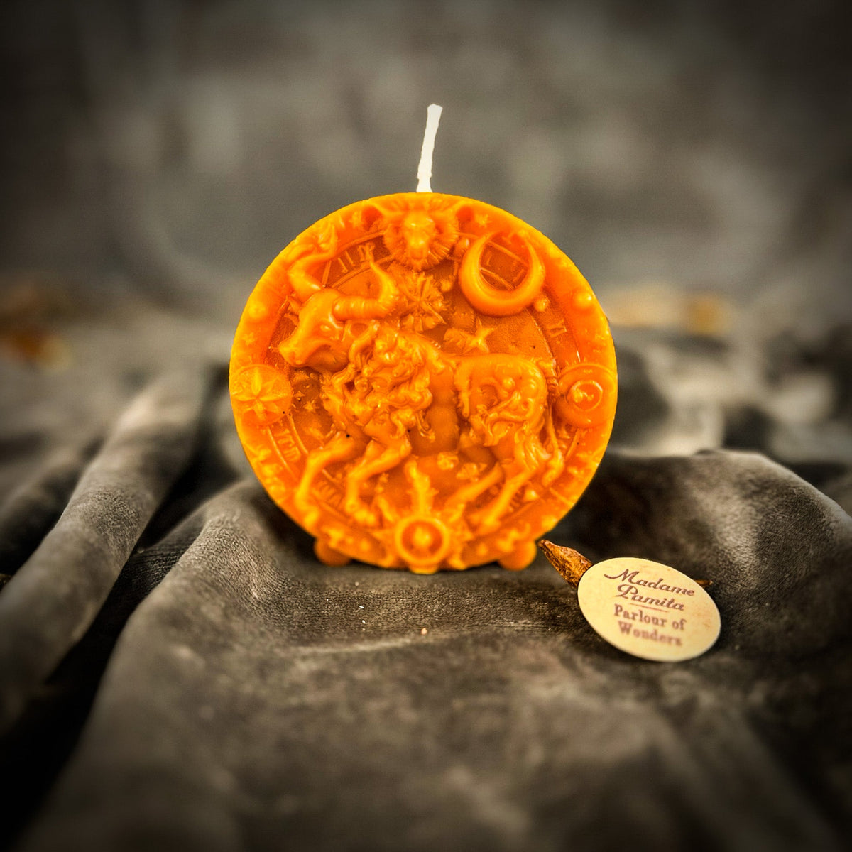 Taurus Bull zodiac spell candle in orange on draped gray fabric