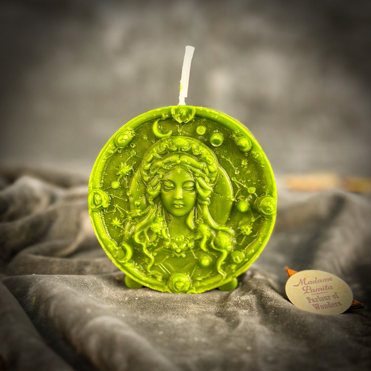 Yellow-green Virgo medallion candle upright on gray velvet, wick unlit.