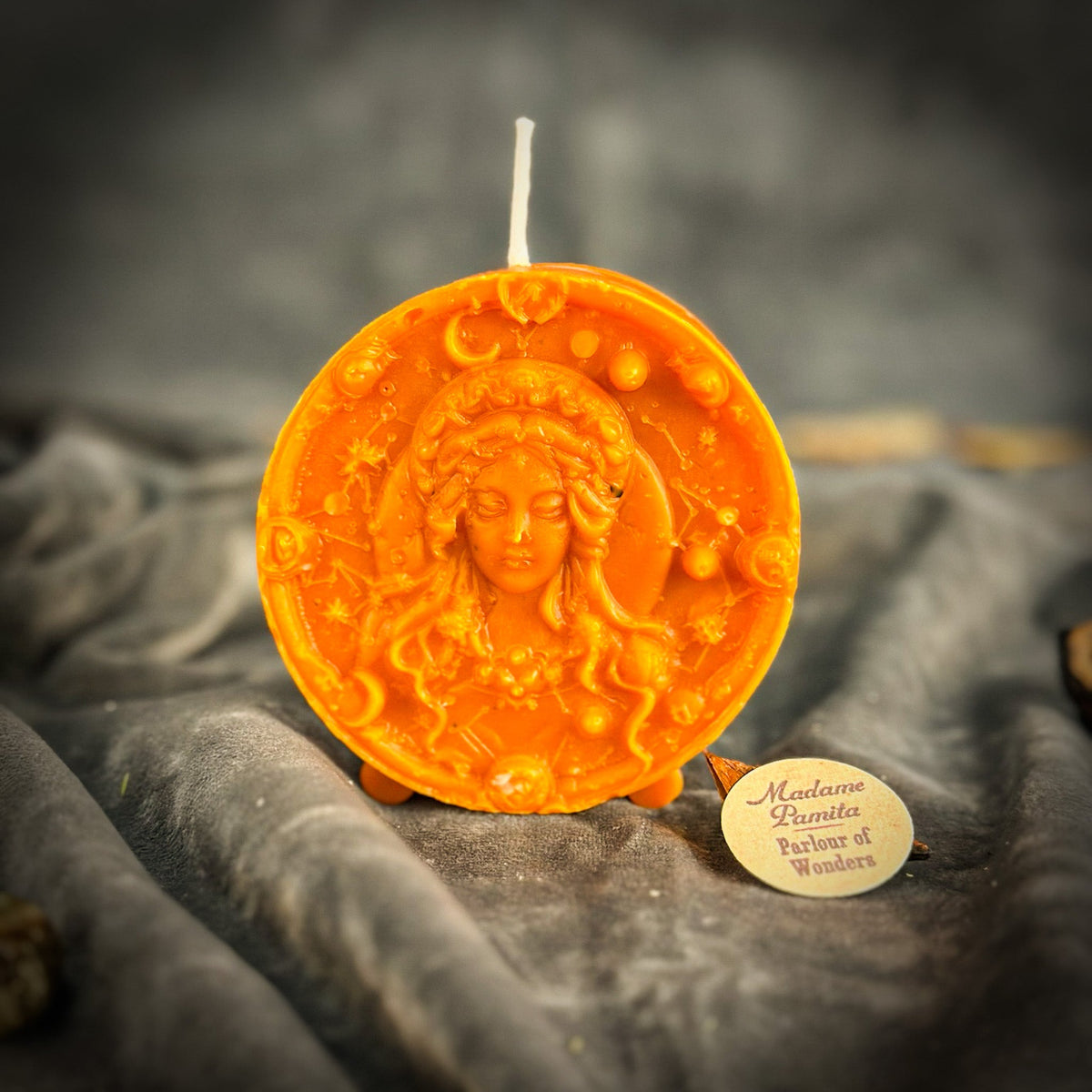Orange Virgo medallion candle, the relief catching a warm side light.