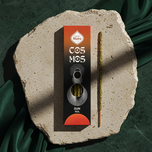 The Sun Cosmos carton and a single incense stick arranged on a pale stone slab over dark green velvet.