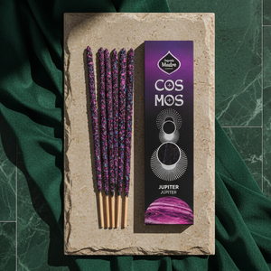 The Jupiter Cosmos carton beside five violet-speckled incense sticks on a pale stone slab over dark green velvet.