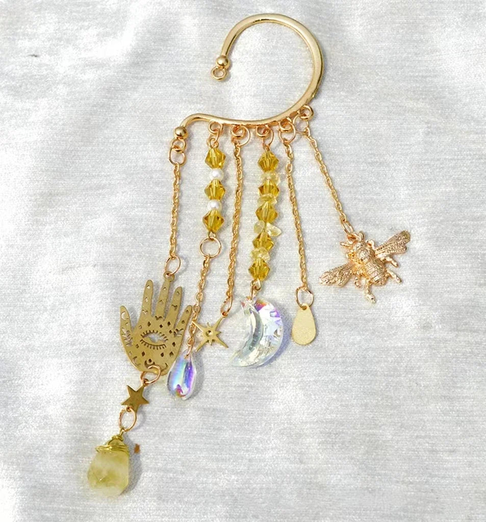 Gold ear cuff earring with sun and moon charms and a long natural quartz crystal drop, worn on one ear — product photo 3