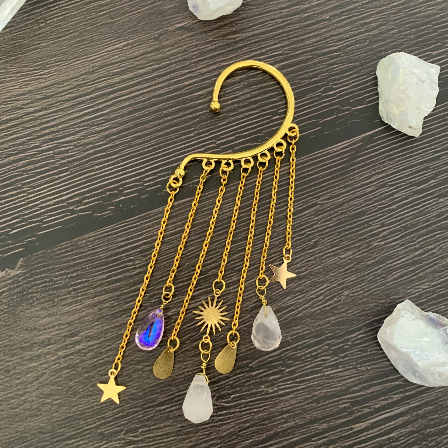 Gold ear cuff earring with sun and moon charms and a long natural quartz crystal drop, worn on one ear — product photo 5