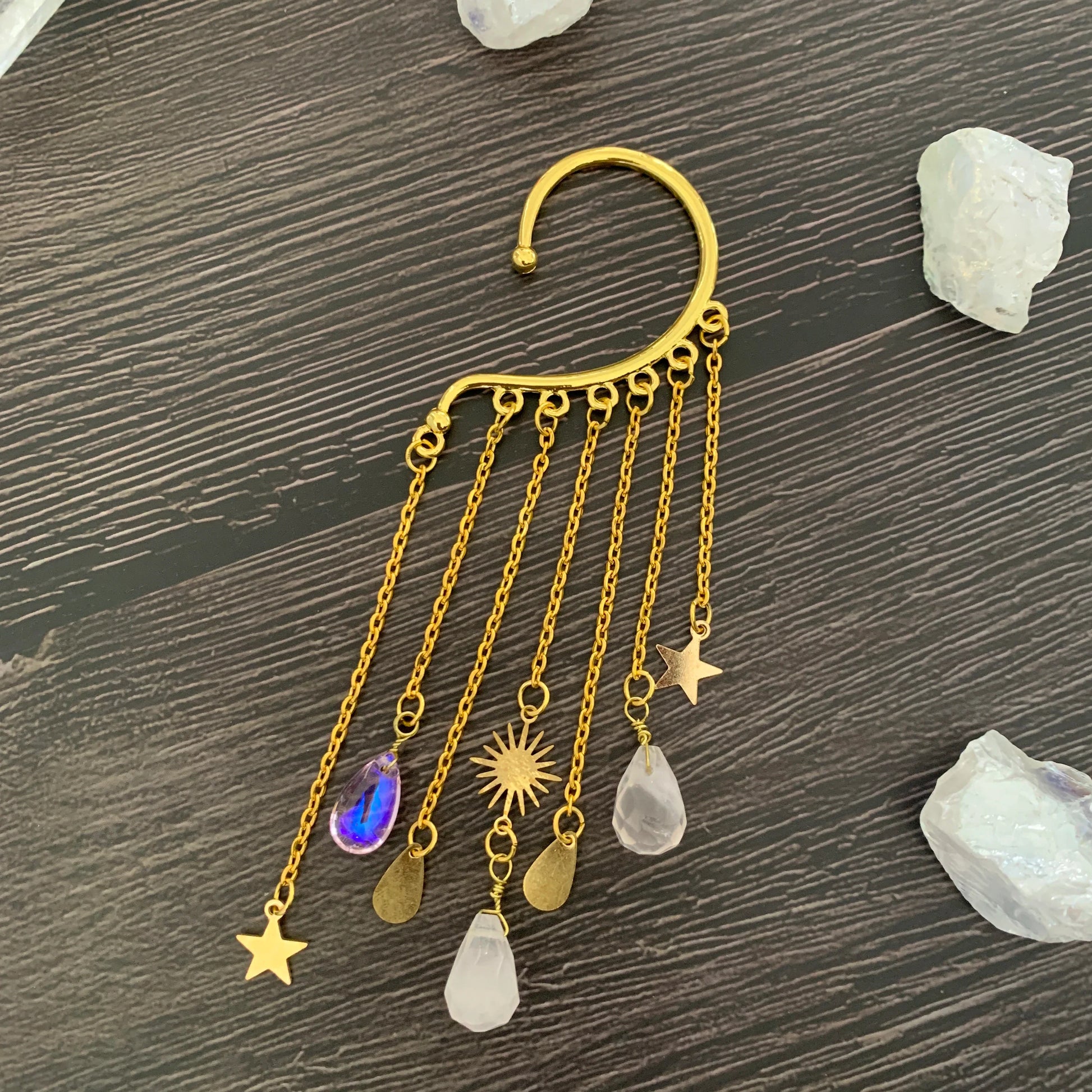 Gold ear cuff earring with sun and moon charms and a long natural quartz crystal drop, worn on one ear — product photo 5