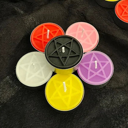 Six pentacle tealights arranged in a ring on black fabric — orange-red, pink, purple, yellow, cream and a black one raised in the middle, each in a metal cup.