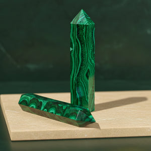 Two malachite points, one upright and one flat, on a sandstone slab against dark green