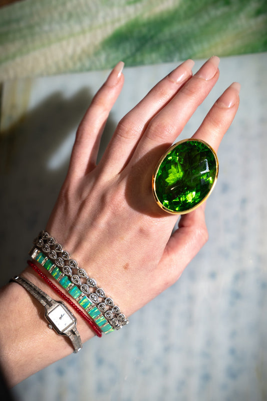 Oval Colossus Ring in Green Envy — oversized faceted green glass oval in a tall gold-plated setting on a wide band