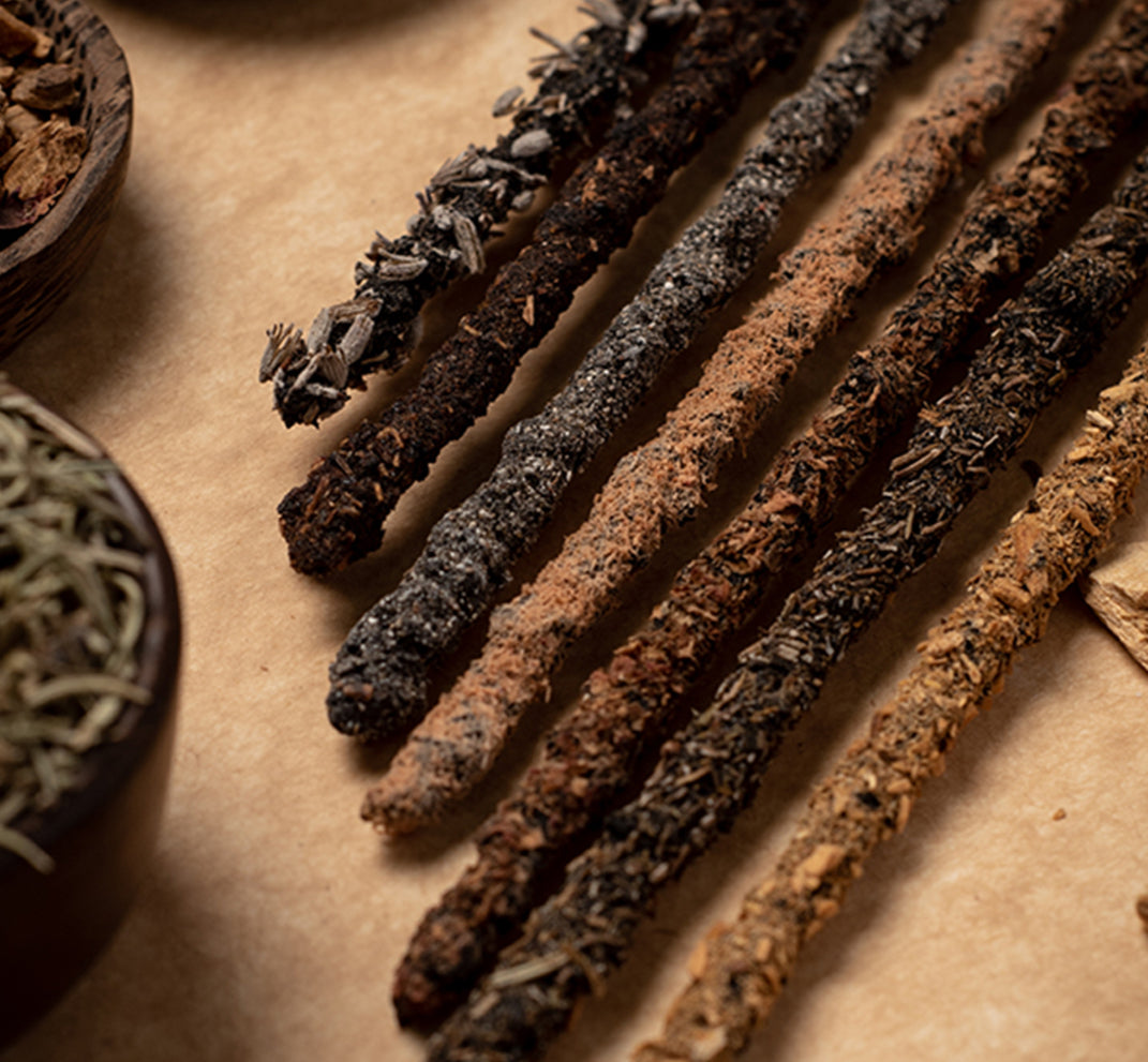 Close-up of the dark hand-rolled chakra incense sticks with loose herbs behind them