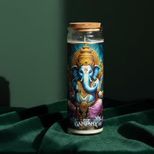 The tall cylindrical glass candle stands on dark green velvet, closed with a cork stopper; the wrap label shows Ganesha, blue-skinned and elephant-headed, seated on lotus petals beneath a gold crown, with GANESHA printed below.