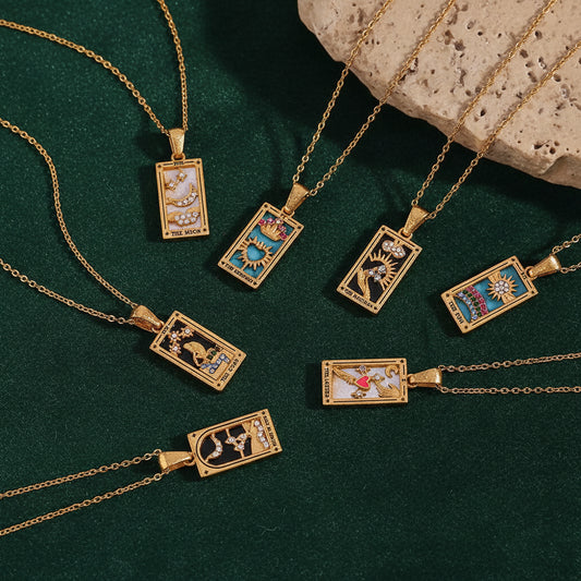 Seven gold tarot card necklaces fanned out on dark green velvet beside a travertine block — The Moon, The Empress, The Magician, The Sun, The Star, The Lovers and Knight of Cups.