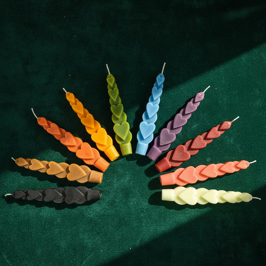 Ten Love Spell Heart Taper candles fanned out in a half circle on dark green velvet: black, brown, burnt orange, golden yellow, olive green, light blue, mauve, brick red, coral and cream.