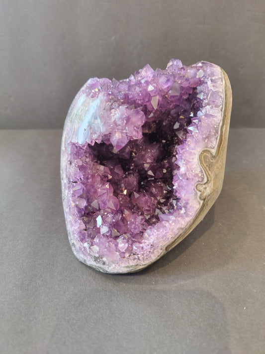 Polished-edge amethyst geode sculpture from Brazil with a stalactite formation inside the purple crystal cavity, 1.25 kilograms
