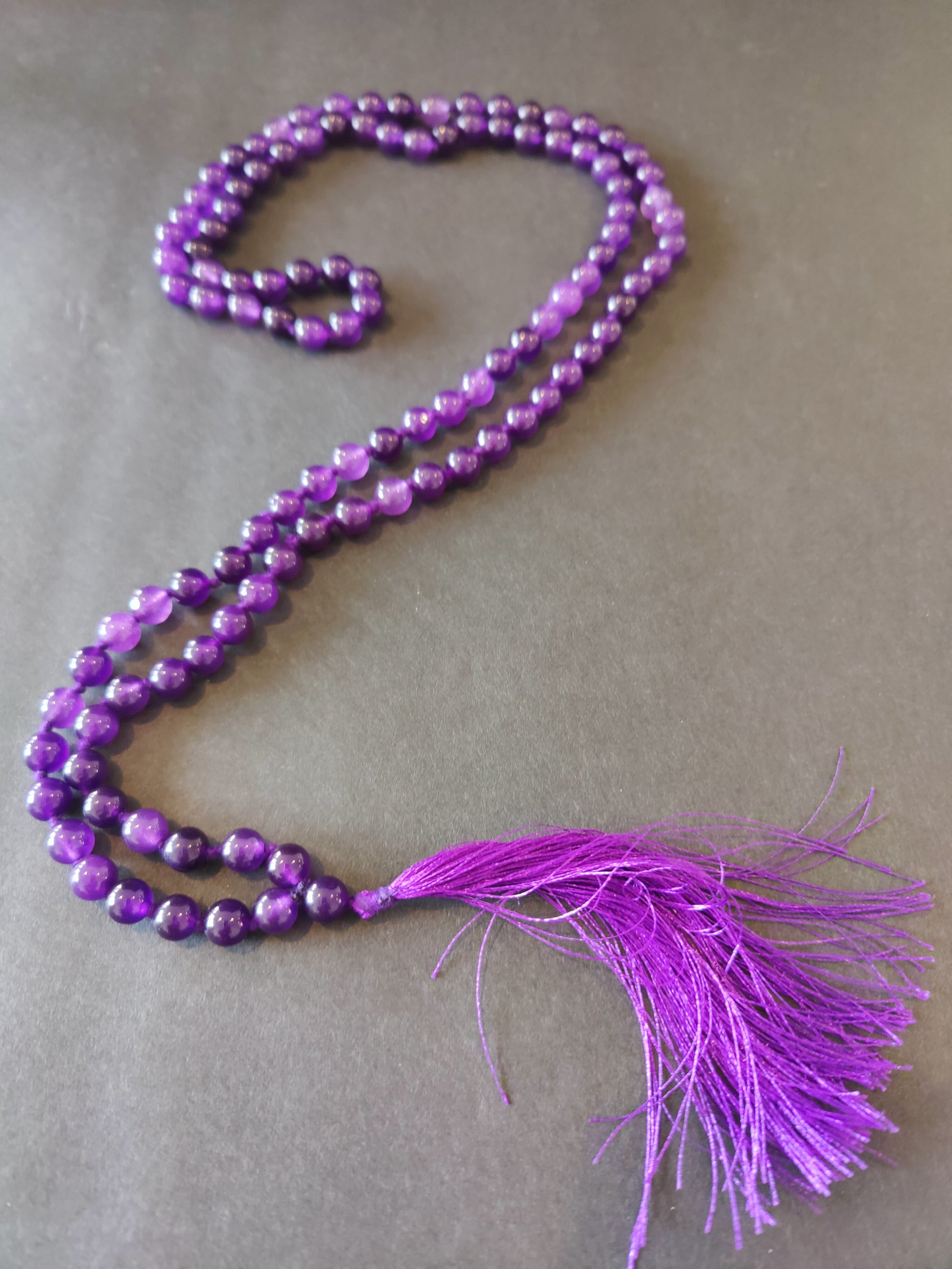 Long mala necklace strung with assorted natural stone beads, hanging in a loop — view 2