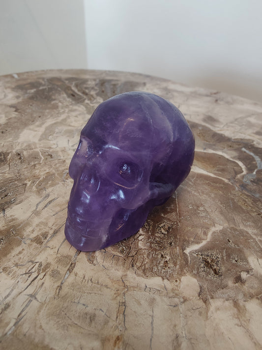 Carved purple fluorite crystal skull with banded violet and clear zones, front three-quarter view