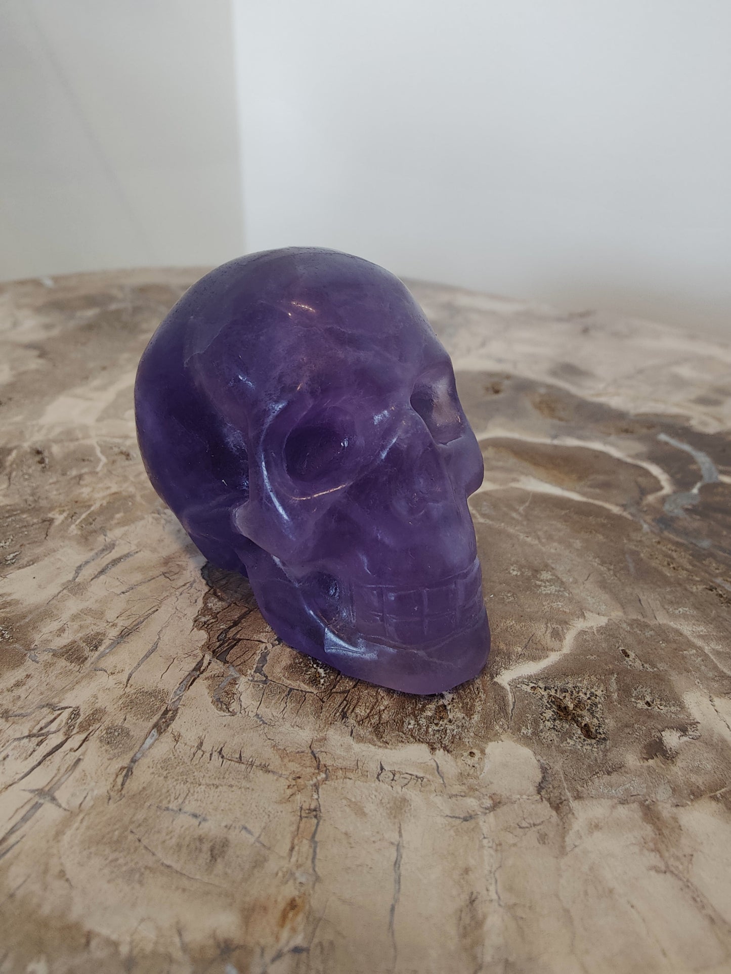 Carved purple fluorite crystal skull with banded violet and clear zones, front three-quarter view — view 2