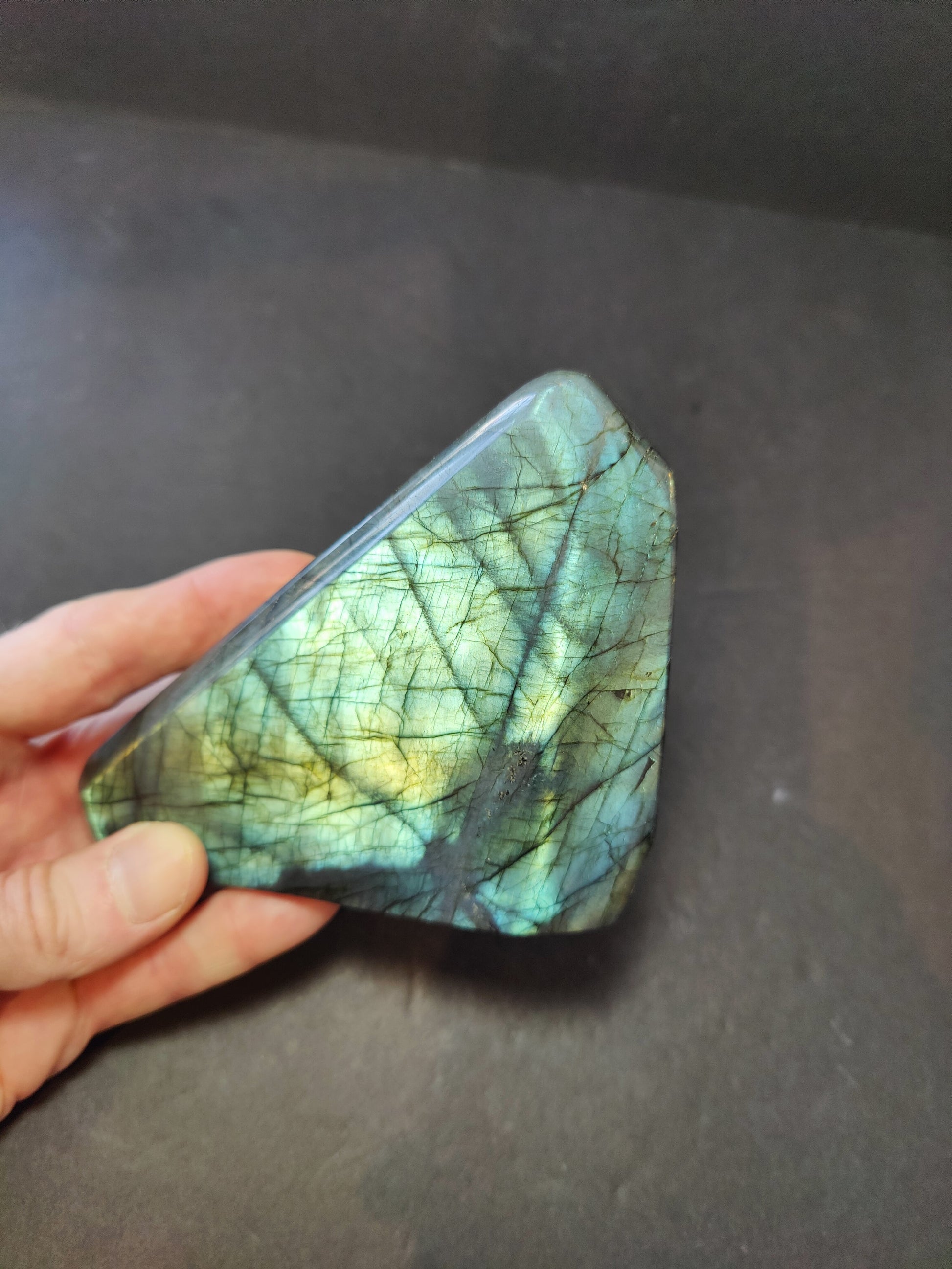 Polished labradorite freeform sculpture from Madagascar showing blue and gold flash across a grey stone surface — view 2