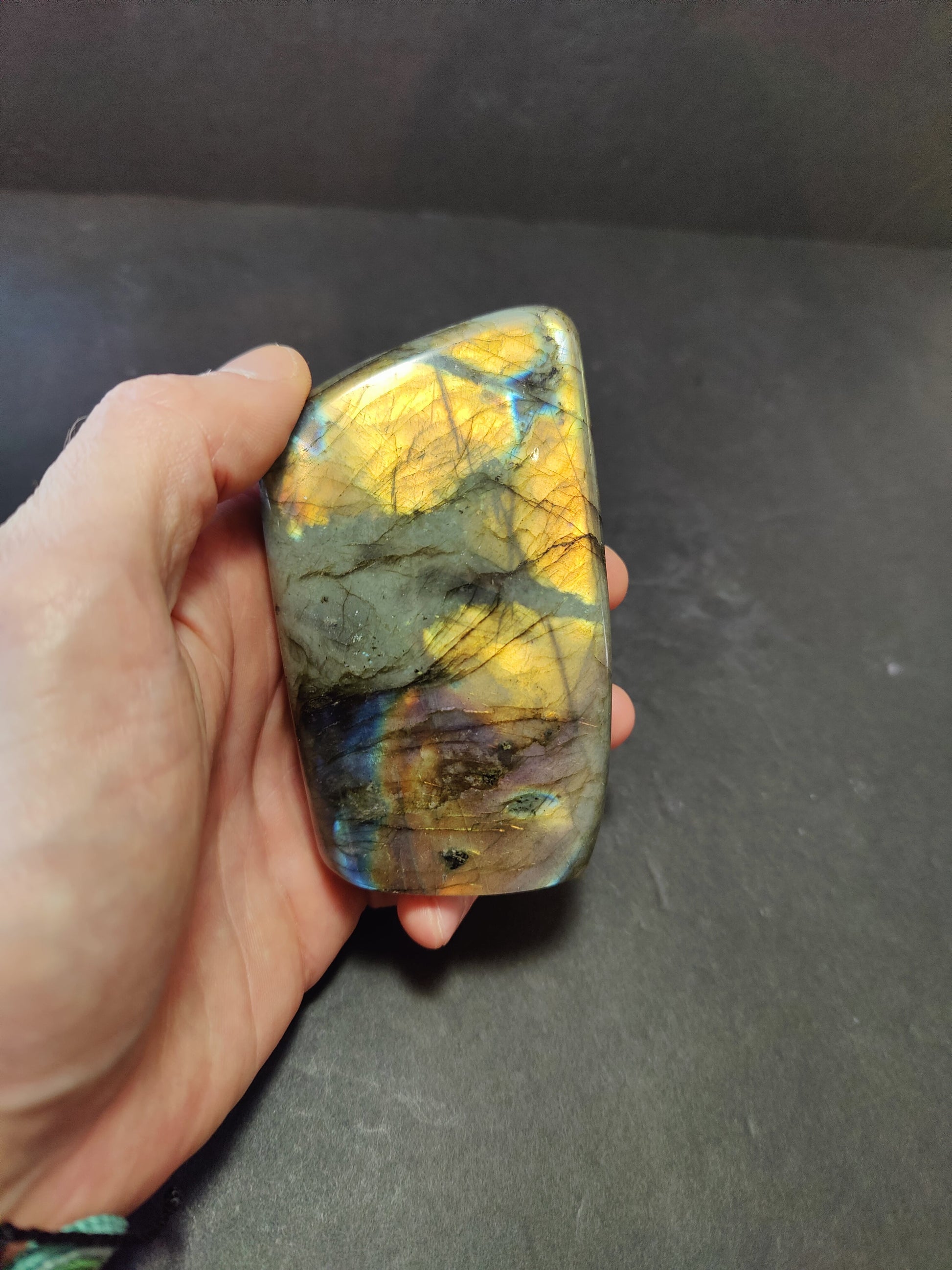 Polished labradorite freeform sculpture from Madagascar showing blue and gold flash across a grey stone surface — view 3