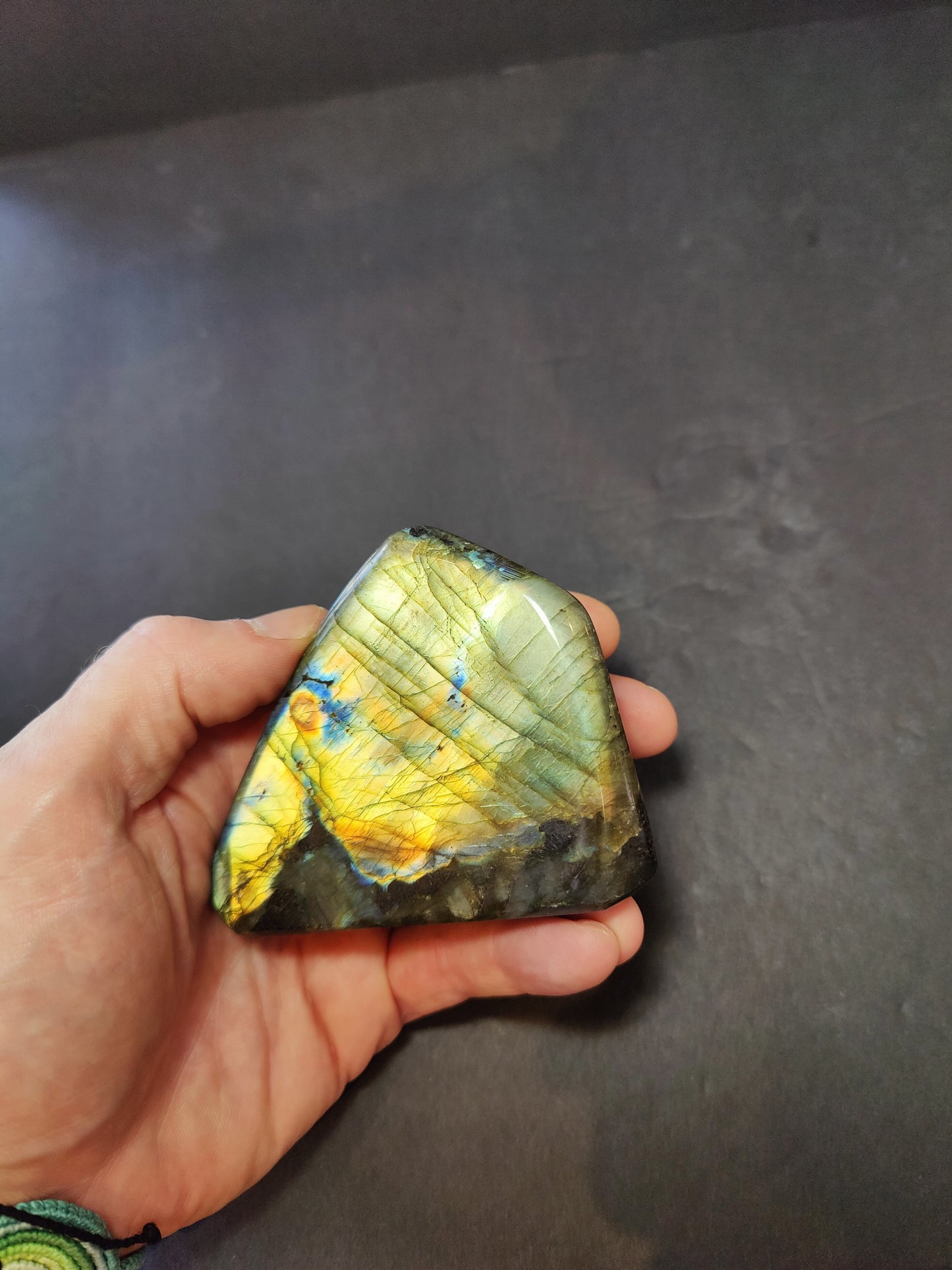 Polished labradorite freeform sculpture from Madagascar showing blue and gold flash across a grey stone surface — view 4