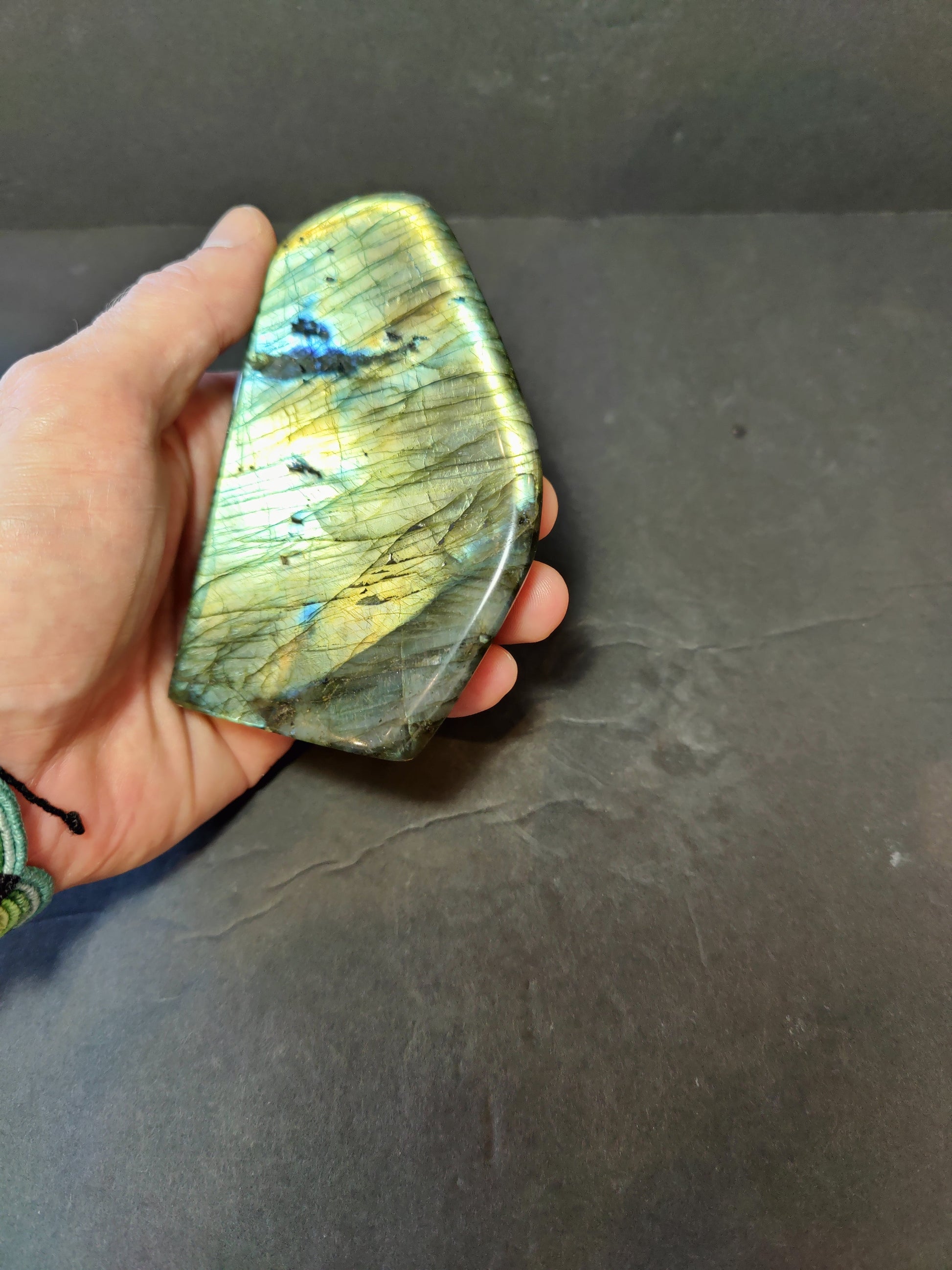 Polished labradorite freeform sculpture from Madagascar showing blue and gold flash across a grey stone surface — view 5