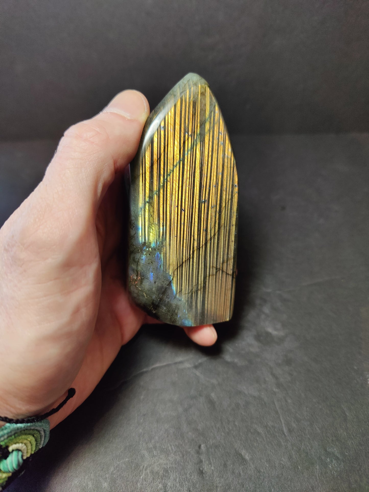 Polished labradorite freeform sculpture from Madagascar showing blue and gold flash across a grey stone surface — view 6