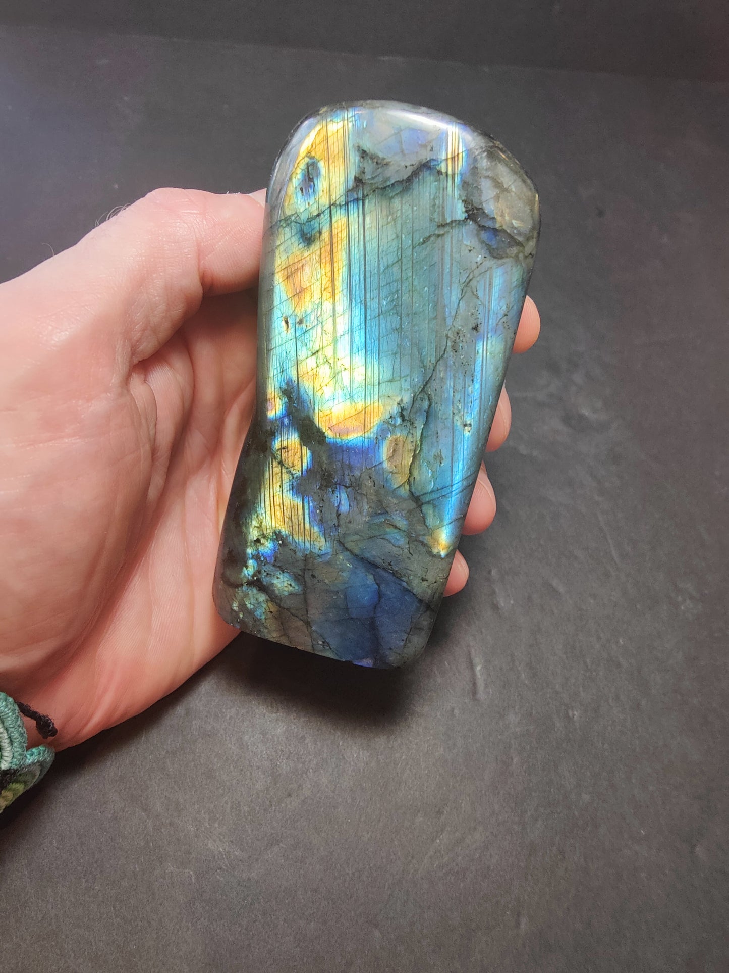Polished labradorite freeform sculpture from Madagascar showing blue and gold flash across a grey stone surface — view 7