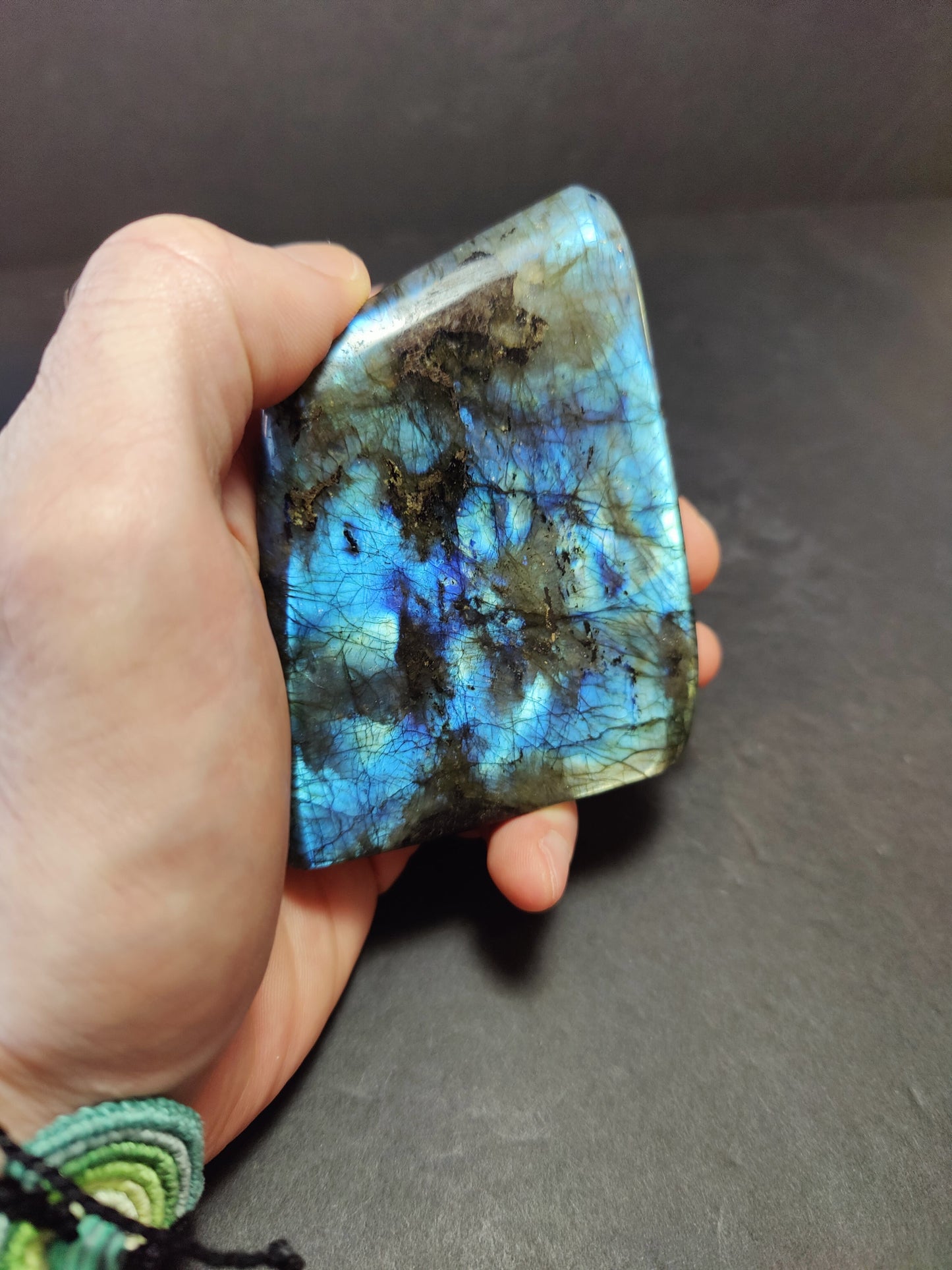 Polished labradorite freeform sculpture from Madagascar showing blue and gold flash across a grey stone surface — view 8