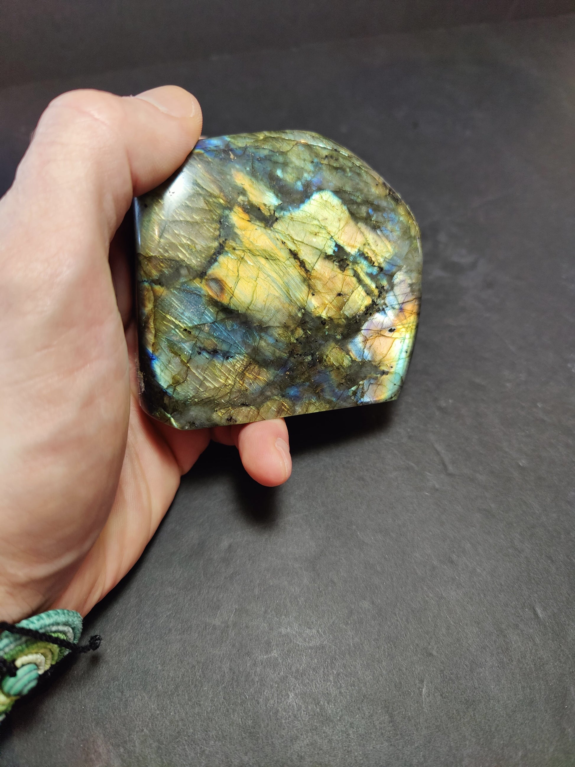 Polished labradorite freeform sculpture from Madagascar showing blue and gold flash across a grey stone surface — view 9