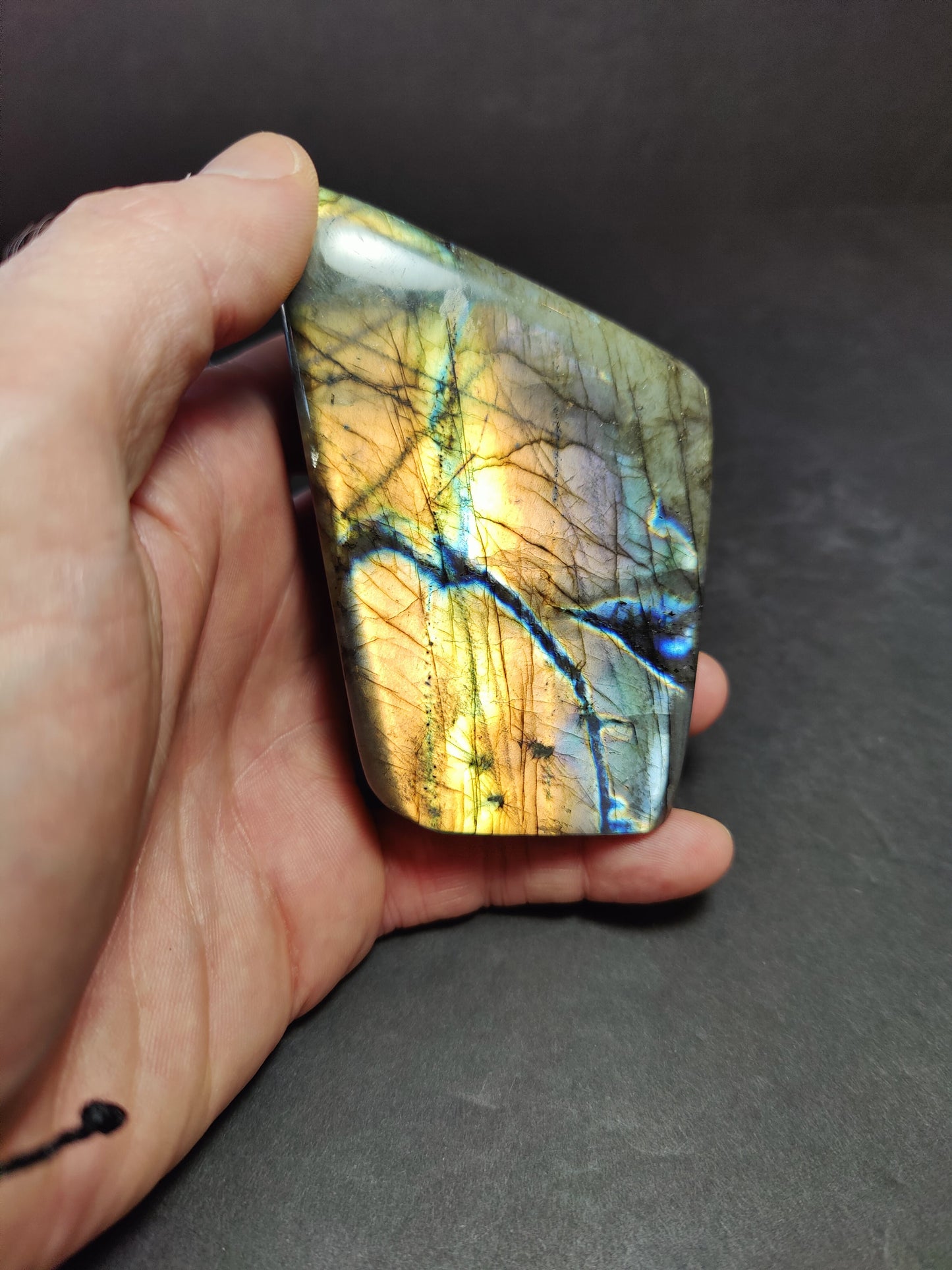Polished labradorite freeform sculpture from Madagascar showing blue and gold flash across a grey stone surface — view 10