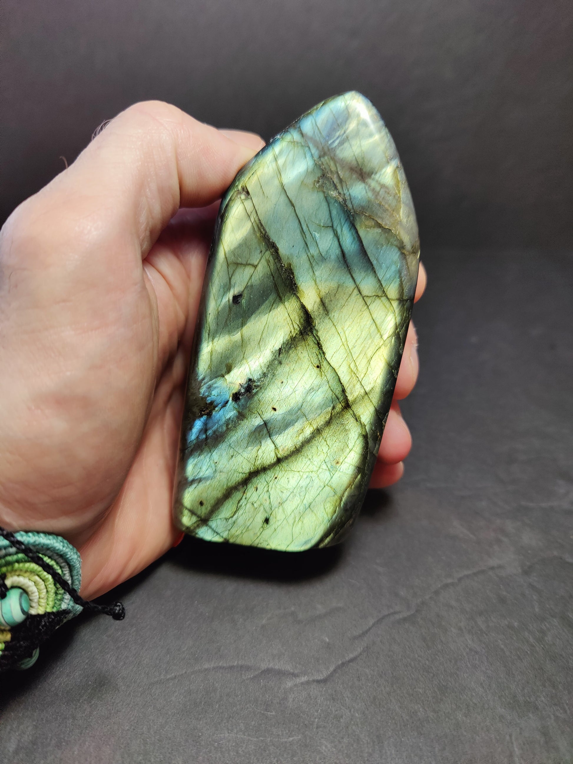 Polished labradorite freeform sculpture from Madagascar showing blue and gold flash across a grey stone surface — view 11