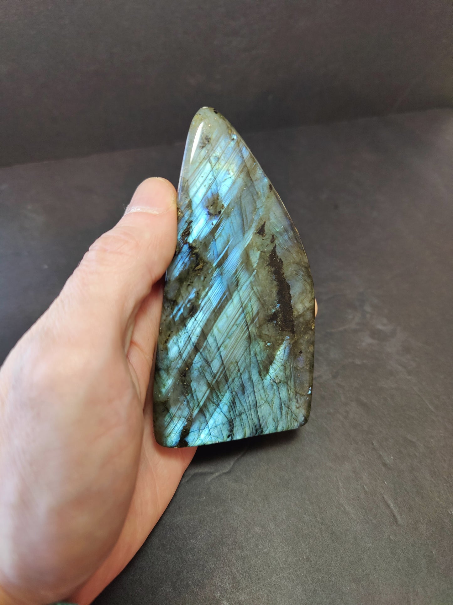 Polished labradorite freeform sculpture from Madagascar showing blue and gold flash across a grey stone surface — view 12