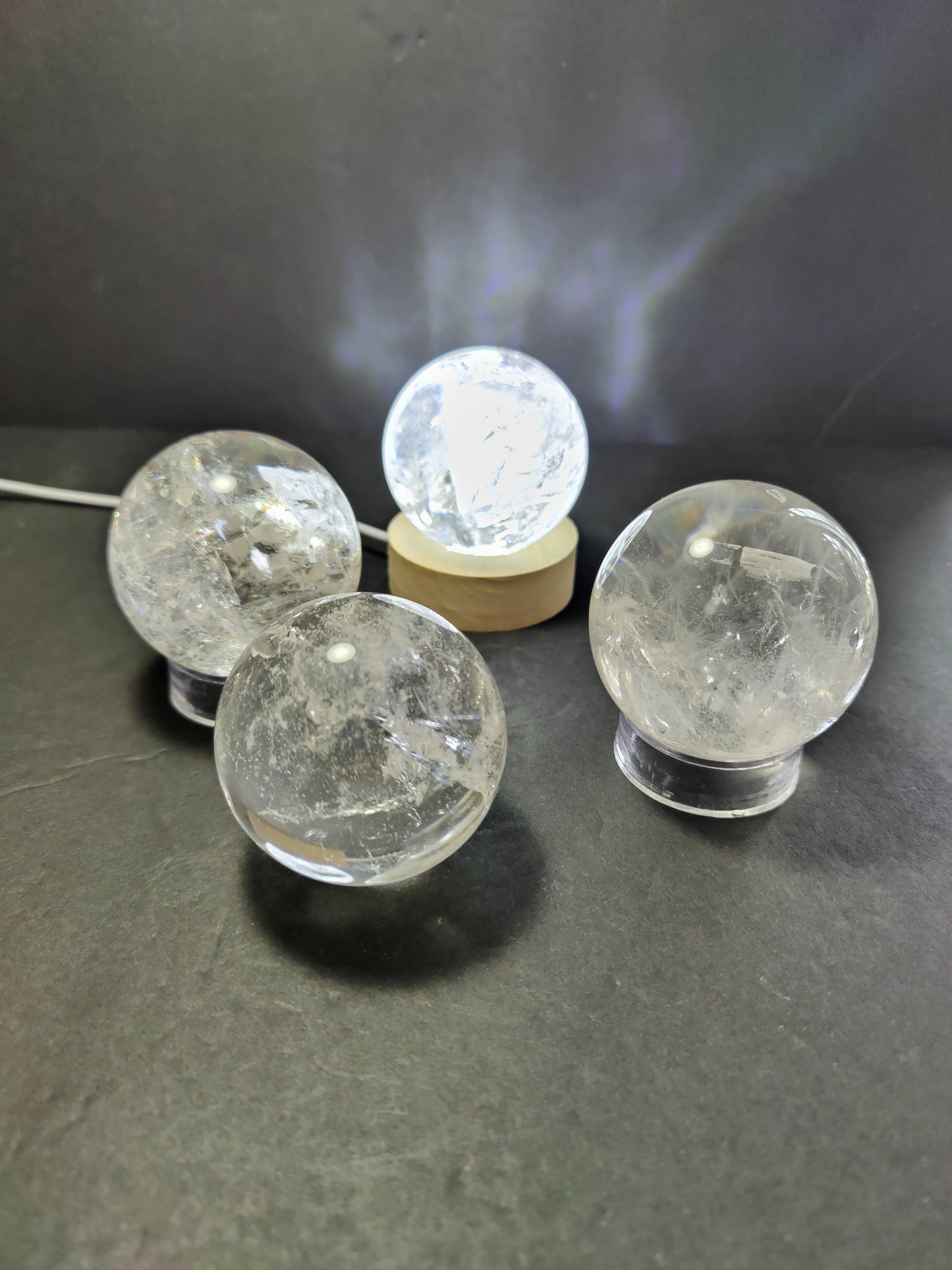 Polished clear quartz crystal sphere catching the light, with natural internal veils — view 2