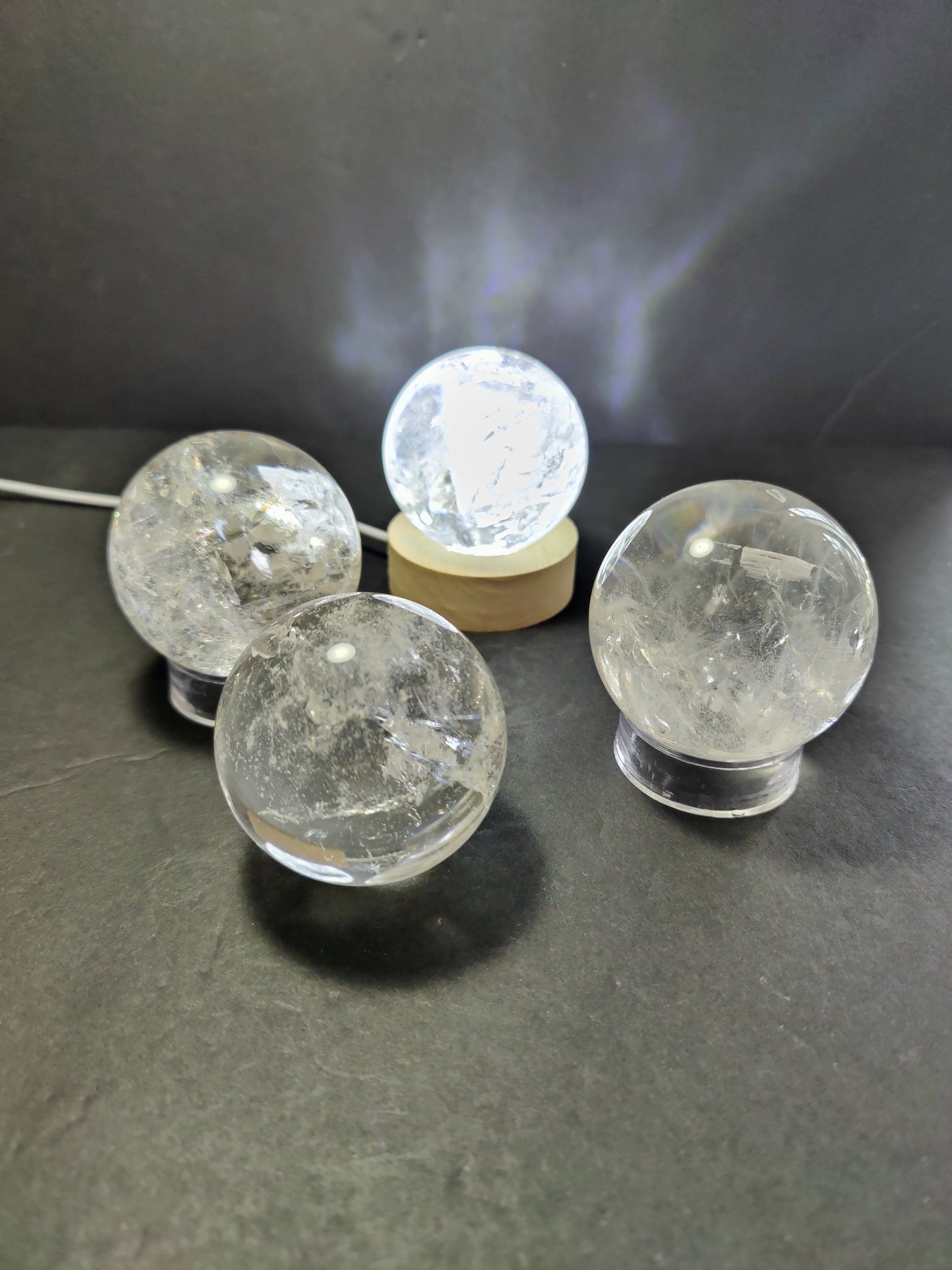 Polished clear quartz crystal sphere catching the light, with natural internal veils — view 2