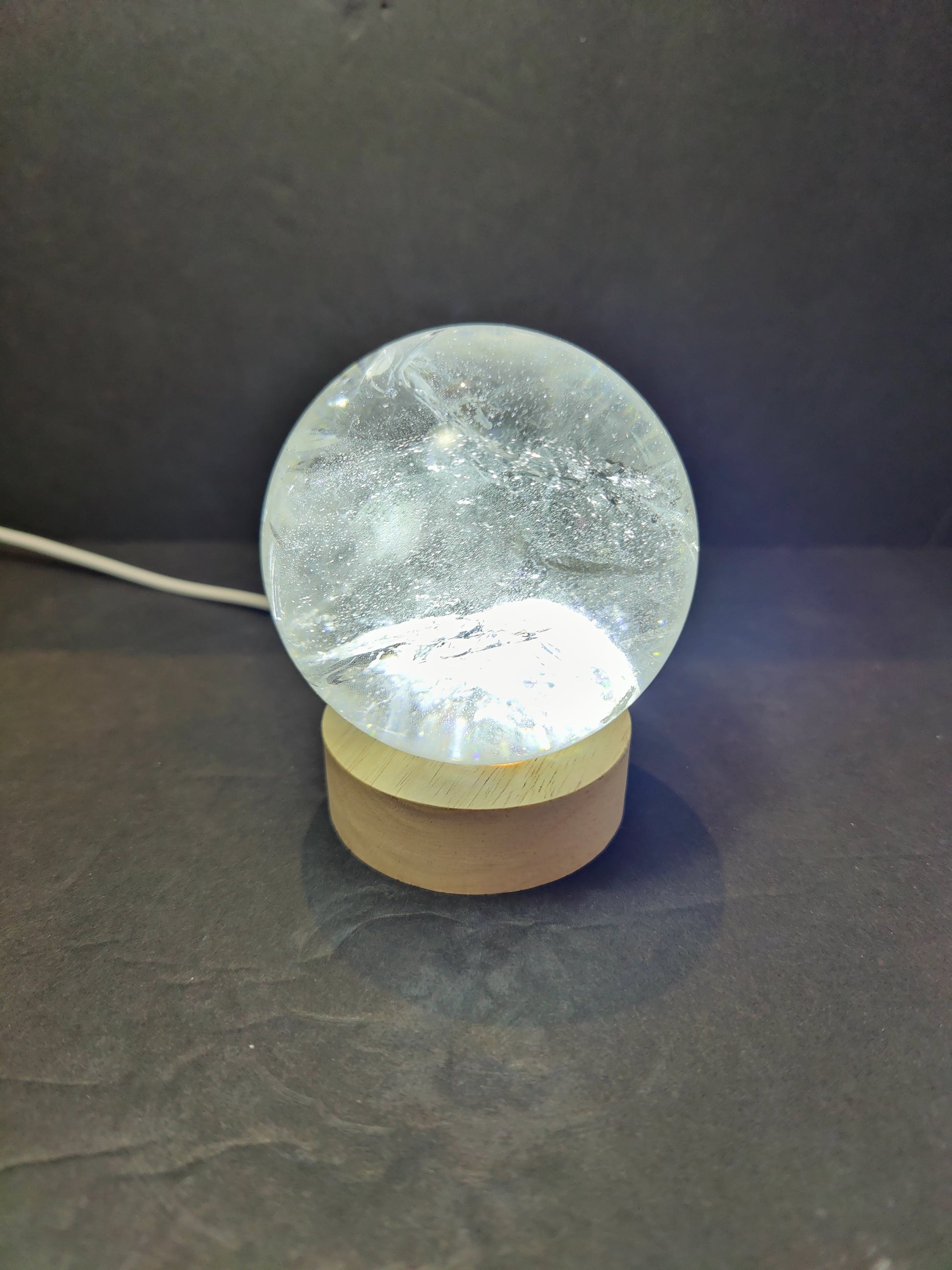Polished clear quartz crystal sphere catching the light, with natural internal veils — view 4
