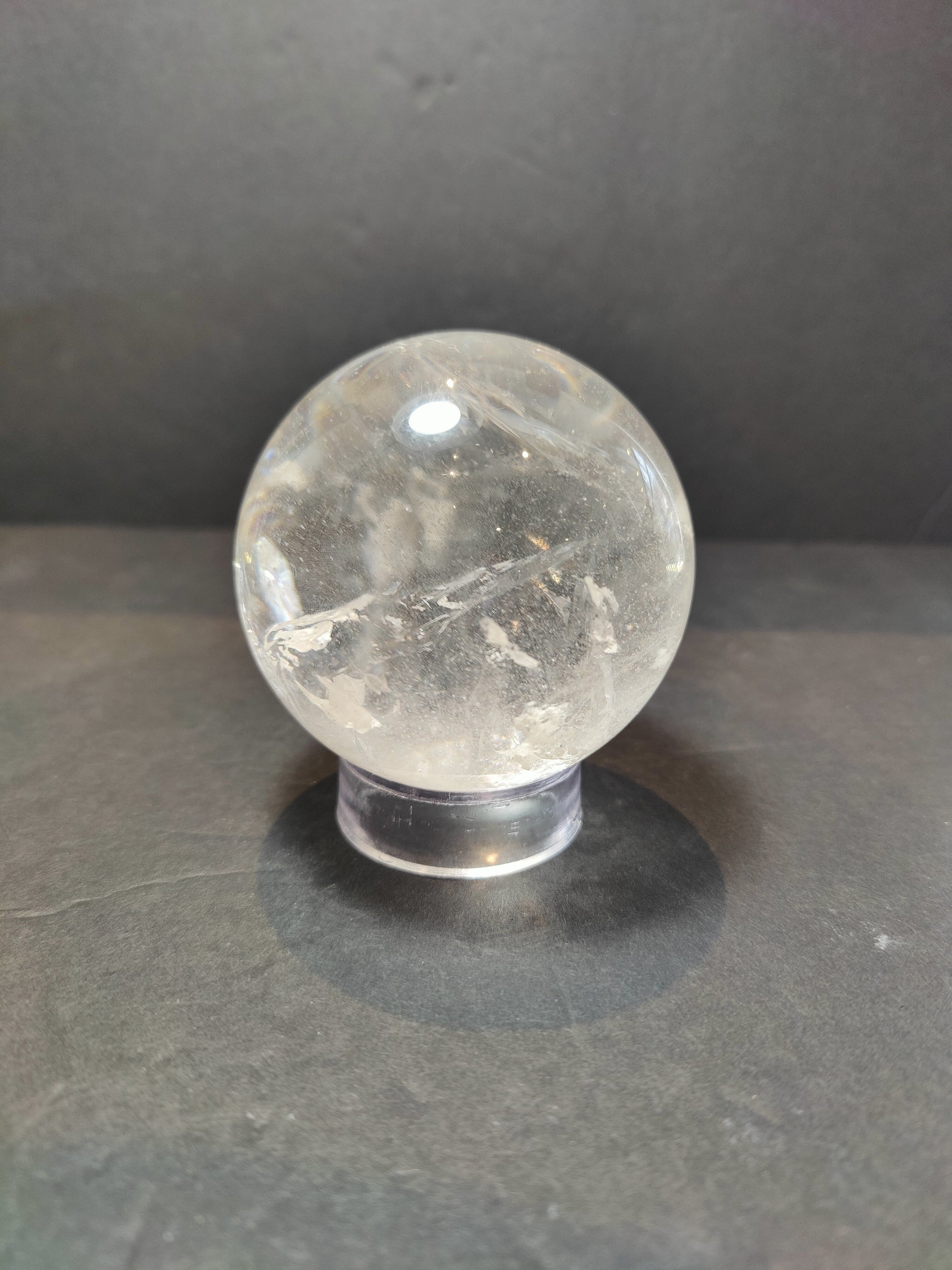 Polished clear quartz crystal sphere catching the light, with natural internal veils — view 3