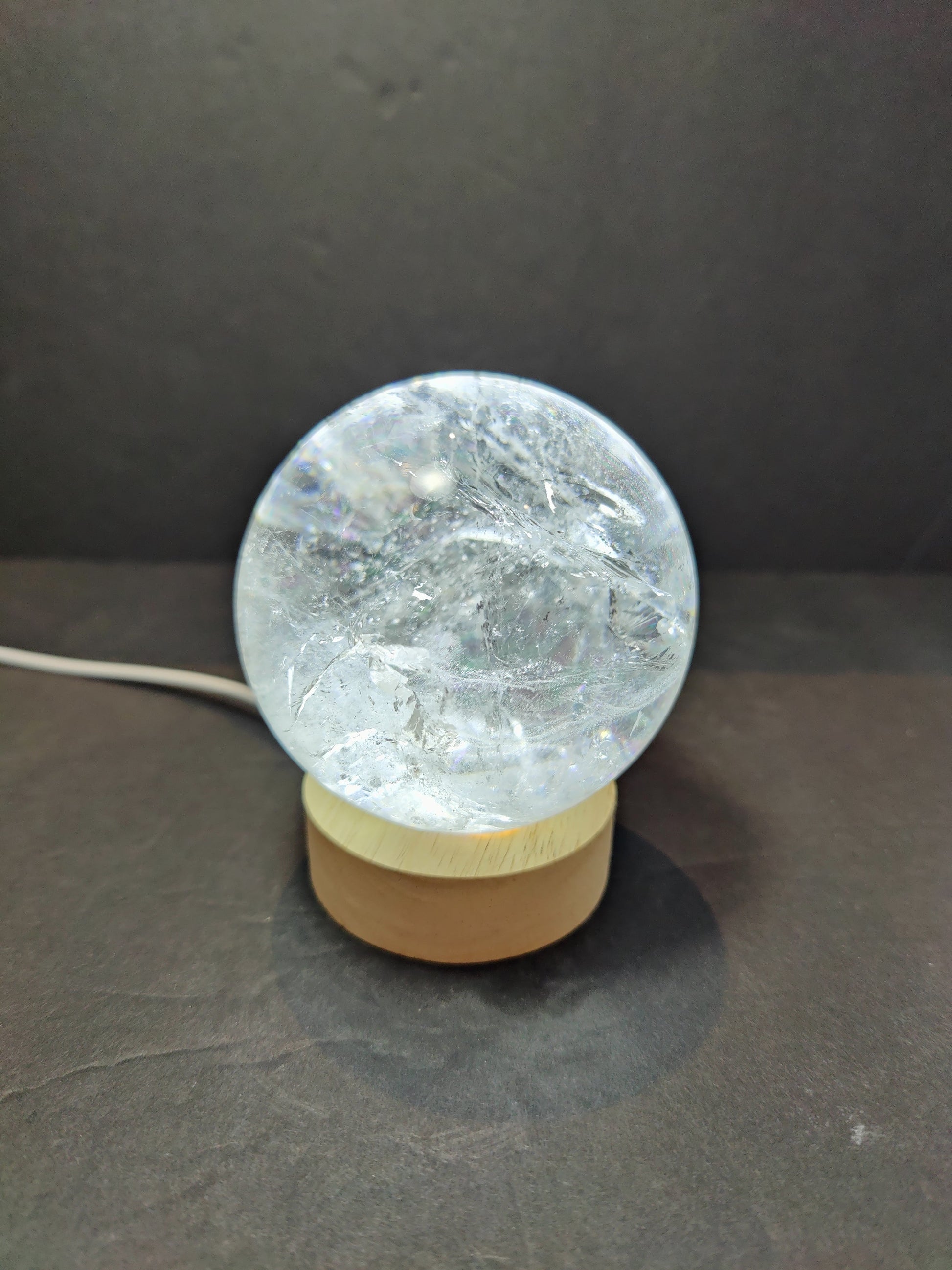 Polished clear quartz crystal sphere catching the light, with natural internal veils — view 6