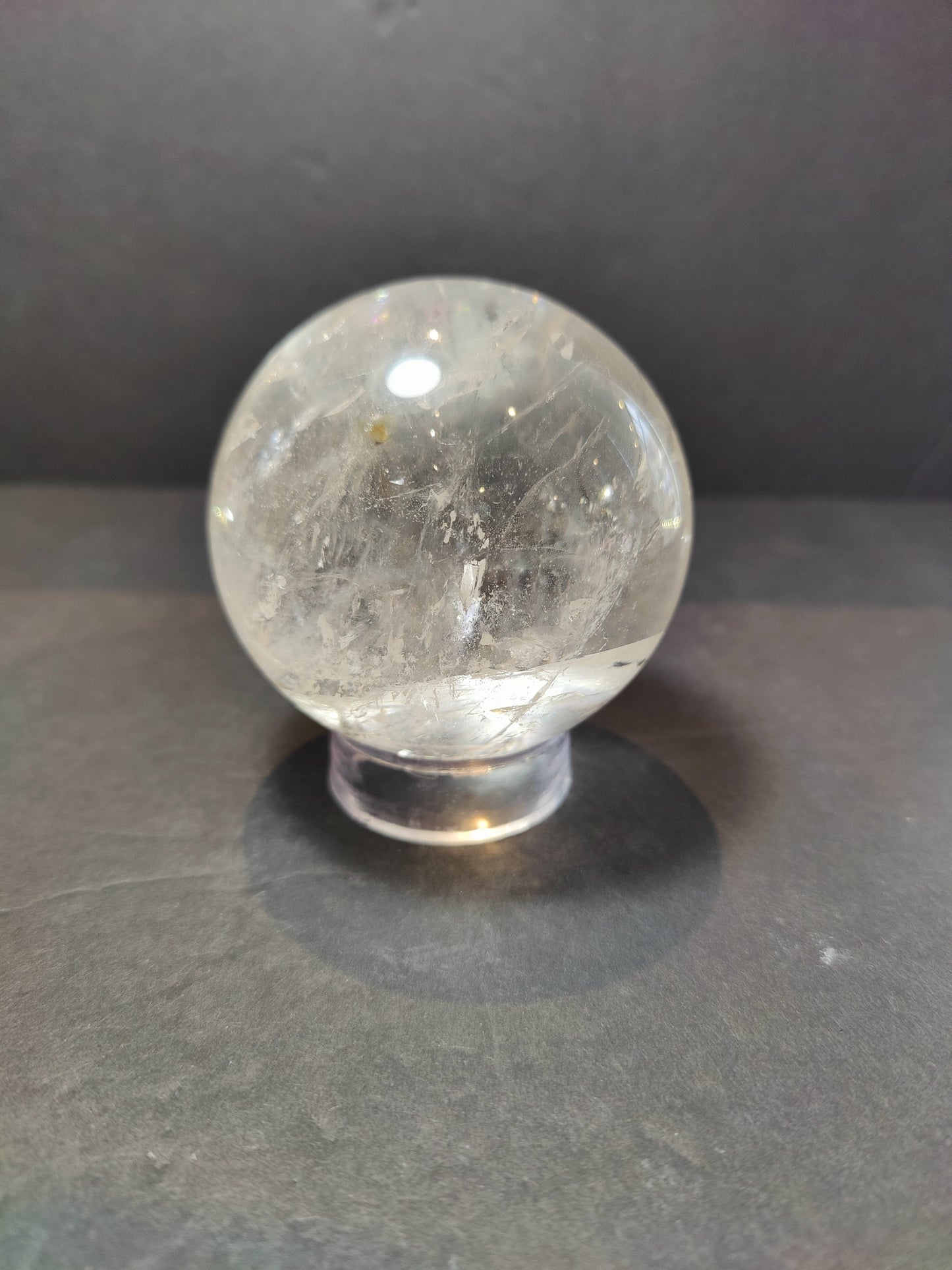 Polished clear quartz crystal sphere catching the light, with natural internal veils — view 5